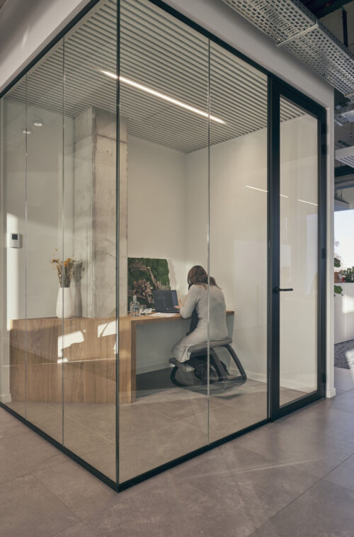 Een kantoor met glazen wanden en een persoon die aan een bureau zit.