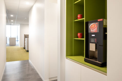 Een koffiezetapparaat in een gang met groene planken. Haal je cafeïneverslaving gemakkelijk in deze levendige hal.
